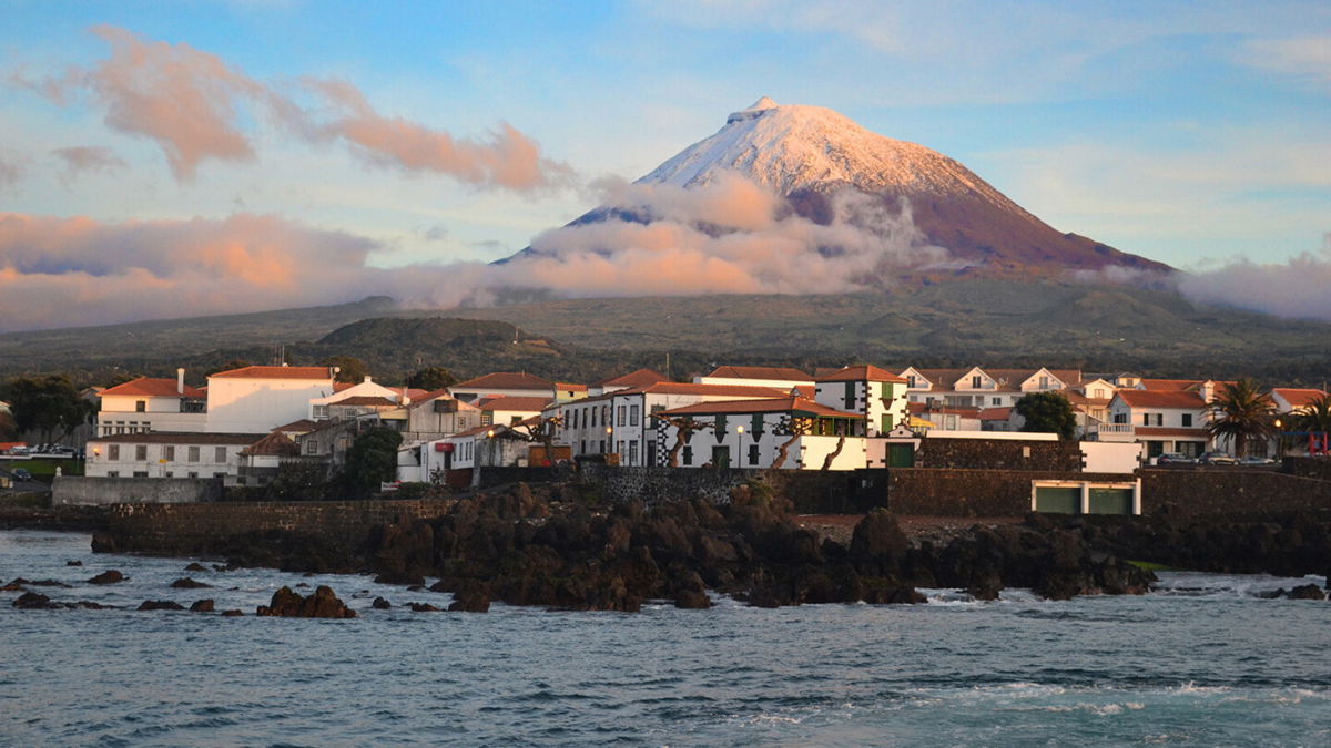 <i>Klara Bakalarova/Adobe Stock</i><br/>The highest mountain of Portugal isn't on the European mainland. It's the Azores volcano Montanha do Pico on the island of Pico. The village Madalena is seen below at sunset.