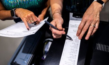 Election judges confirm test vote tallys against a ballot during a public accuracy test of voting equipment on August 3