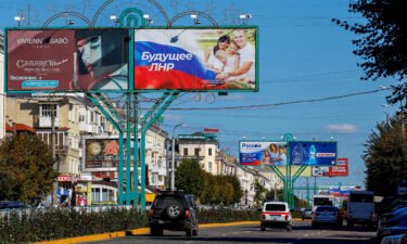 Vehicles drive past advertising boards displaying pro-Russian slogans in a street in Luhansk