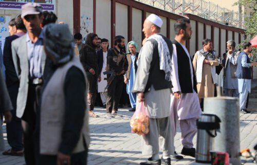 Taliban fighters stand guard as people search for relatives outside a hospital in Kabul on September 30