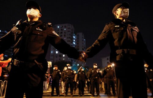 Police officers stand guard as people protest coronavirus restrictions and hold a vigil to commemorate Urumqi fire victims