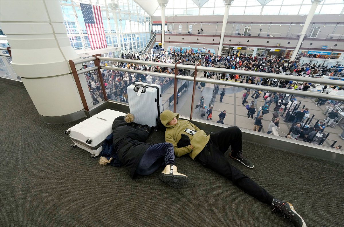 <i>David Zalubowski/AP</i><br/>A pair of travelers sleep while others line up to pass through a security checkpoint in Denver International Airport on Friday.