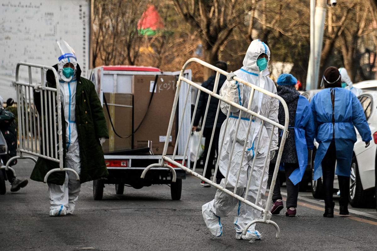 <i>Noel Celis/AFP/Getty Images</i><br/>Health workers carry barricades inside a residential community that reopened following a Covid-19 lockdown in Beijing on December 9