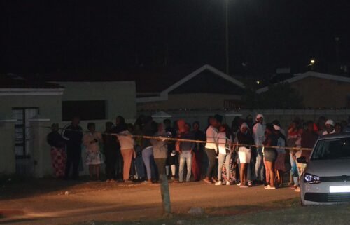 Bystanders wait behind a police tape marking the scene of a mass shooting in Gqeberha