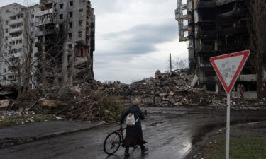 A woman pushes her bicycle in front of a destroyed apartment building in Borodianka