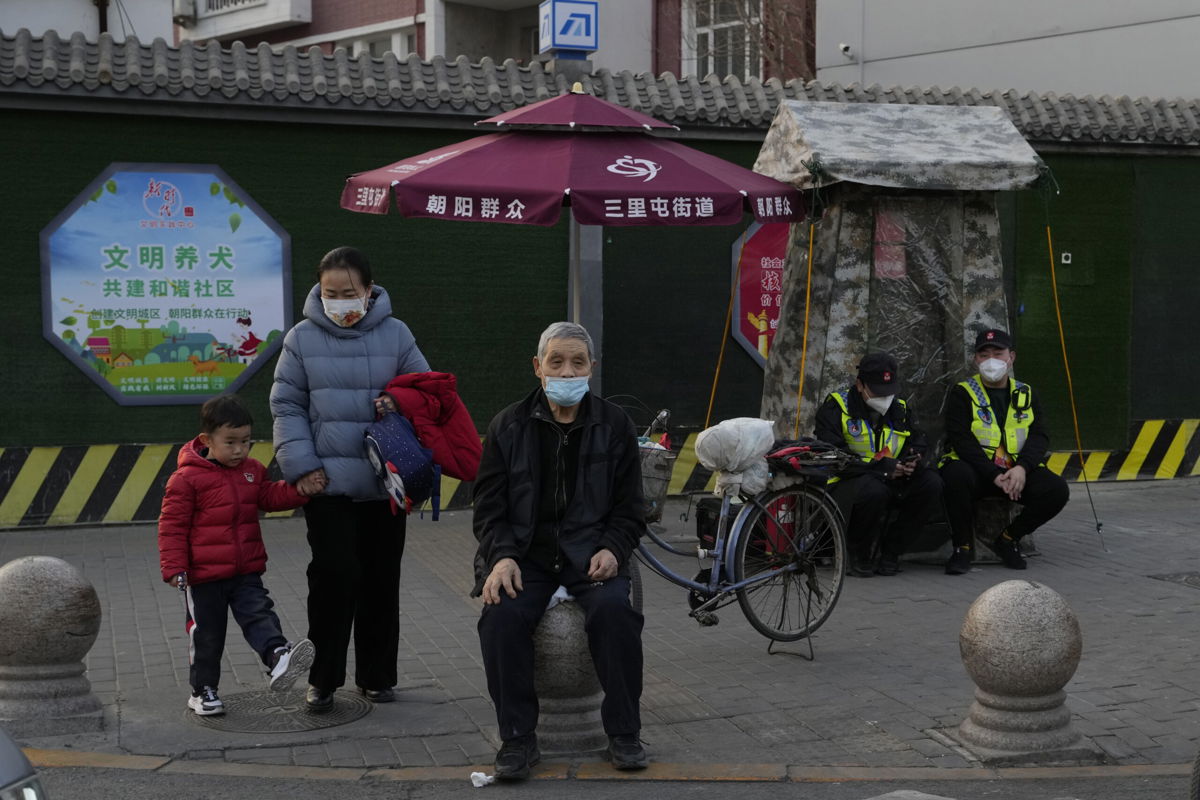 Residents wait to cross a road near members of the Chaoyang militia on duty in Beijing, Monday, March 6, 2023. Chinese economic officials expressed confidence Monday they can meet this year's growth target of 