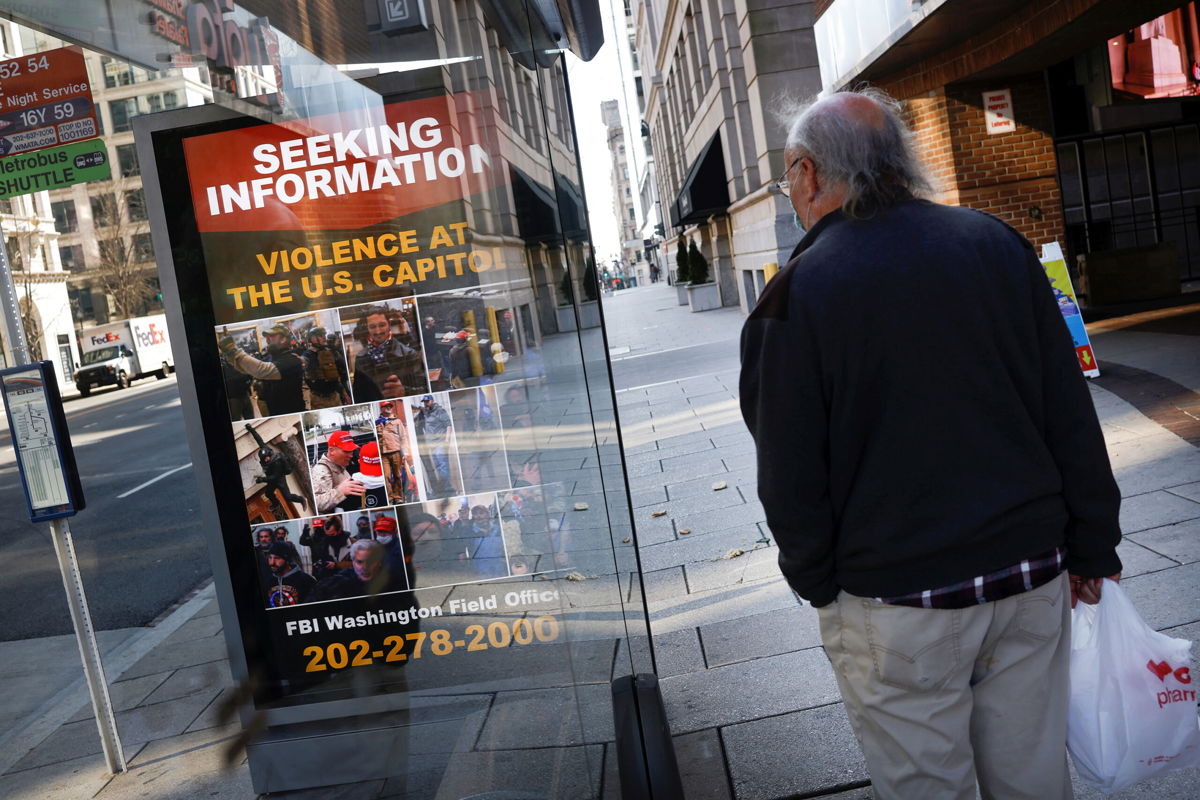 <i>Carlos Barria/Reuters</i><br/>A local resident looks at a billboard with pictures of supporters of Former President Donald Trump wanted by the FBI who participated in storming the US Capitol