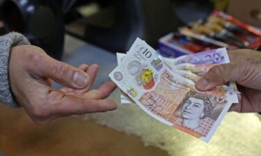 A shopkeeper (left) passes a customer their change in GBP pound sterling ten and twenty pound notes