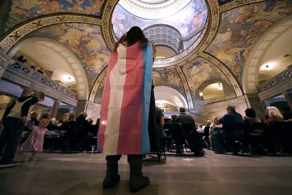 FILE - Glenda Starke wears a transgender flag as a counter protest during a rally in favor of a ban on gender-affirming health care legislation, March 20, 2023, at the Missouri Statehouse in Jefferson City, Mo. A Missouri judge said Friday, Aug. 25, that a law banning gender-affirming treatments for minors can take effect. St. Louis Circuit Judge Steven Ohmer ruled that the law will kick in Monday, Aug. 28, as previously scheduled. 