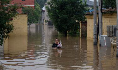 A woman sits next to a flooded road following heavy rains in Zhuozhou