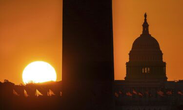 Sunrise behind the Washington Monument and the U.S. Capitol Building illuminates the U.S. flags on the National Mall early Saturday morning