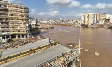 People walk past the body of a flash flood victim in the back of a pickup truck in Derna