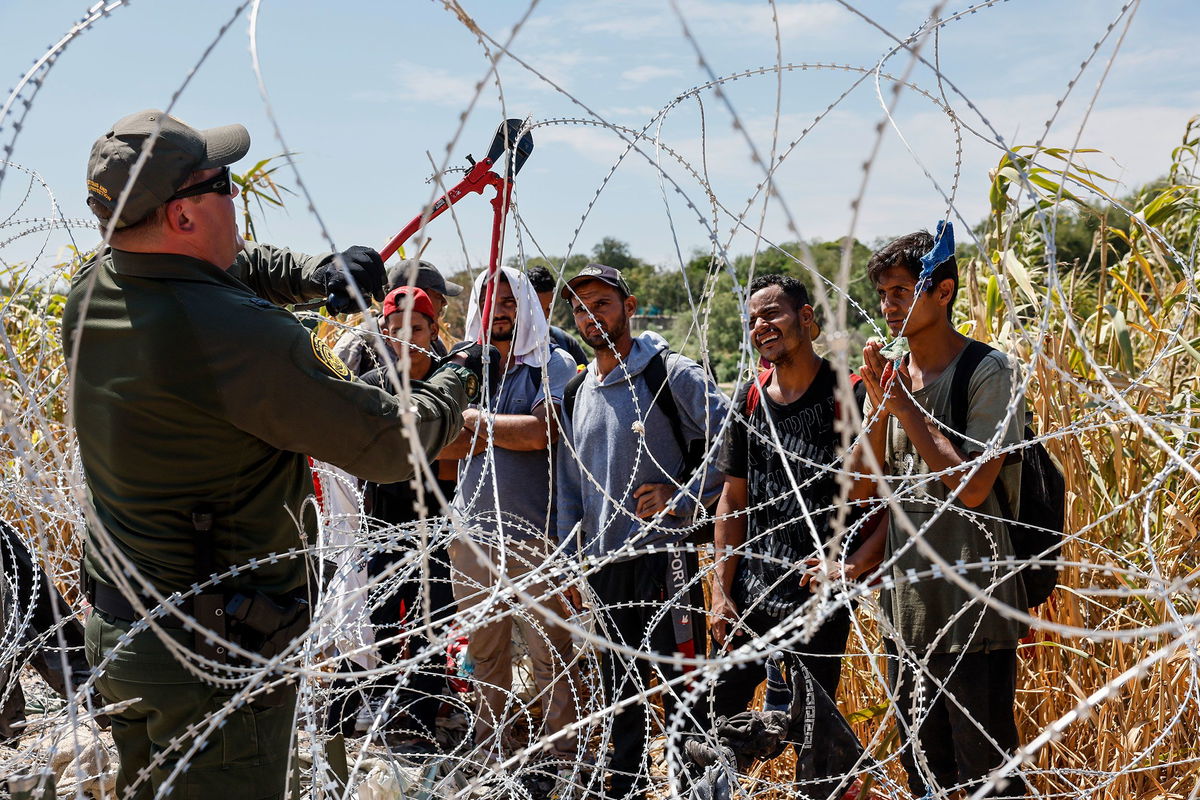 A border patrol agent cuts razor wire to allow migrants who've been waiting in the sun for hours, to come to a way station under the Camino Real International Bridge.
