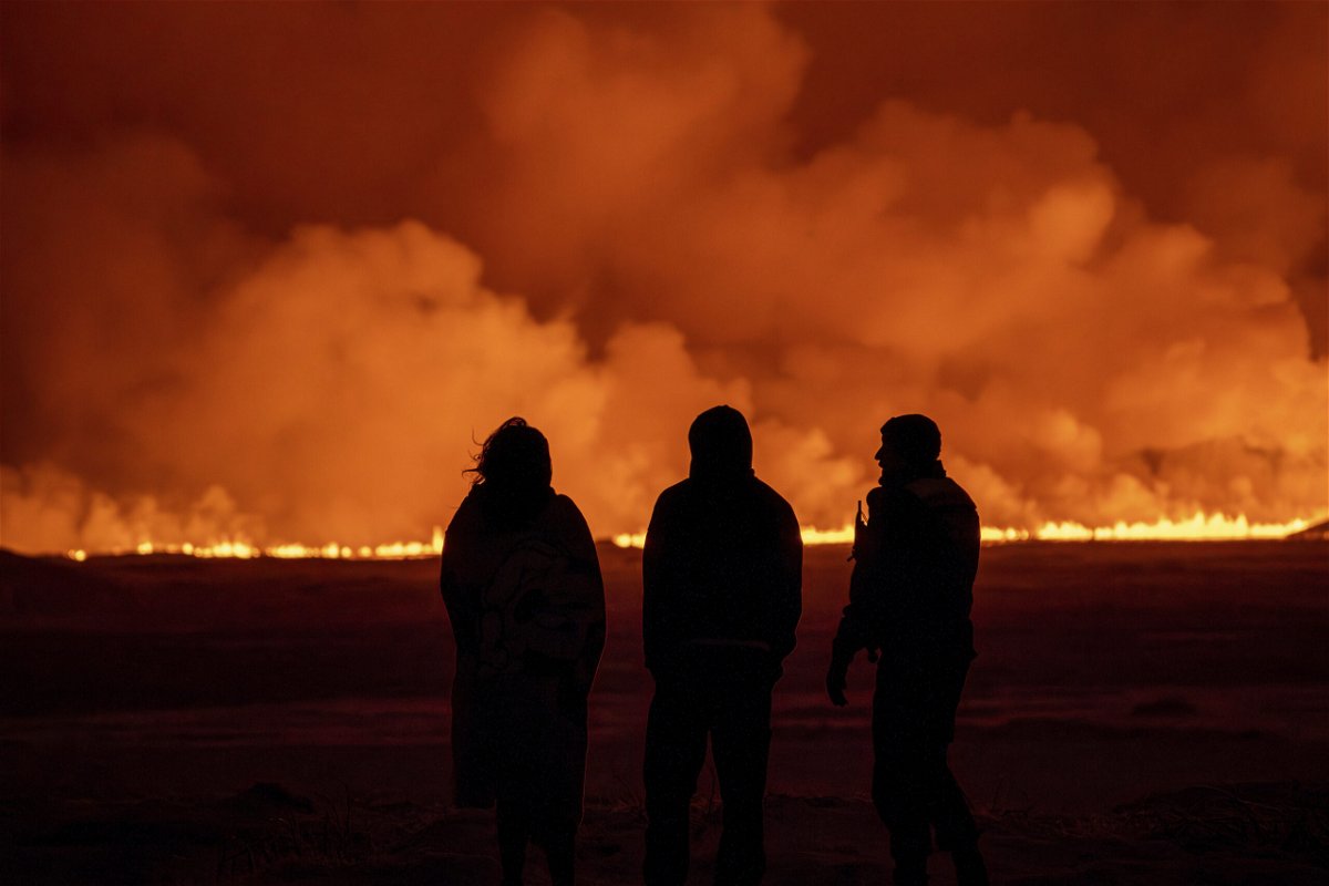 People watch as the night sky is illuminated caused by the eruption of a volcano in Grindavik on Iceland's Reykjanes Peninsula, Monday, Dec. 18, 2023.