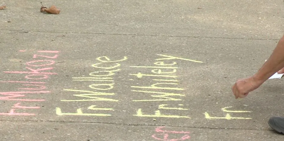 A member of a group representing people who were abuse by priests writes names in chalk on Thursday outside of Immaculate Conception Catholic Church in Jefferson City.