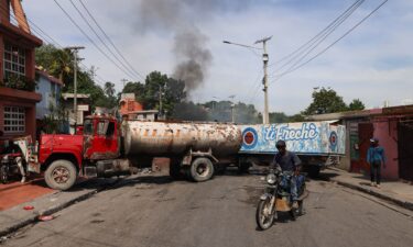 A motorcyclist drives around trucks blocking the road as heavily-armed gangs