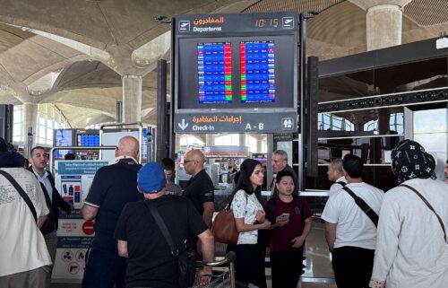 People stand in front of a flight information display screen showing information about delayed and canceled flights at Queen Alia International Airport in Amman